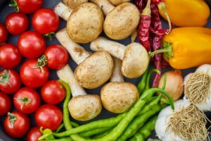 This is a vibrant overhead close-up of a variety of fresh produce, including bright red cherry tomatoes clustered on the left and large yellow bell peppers on the right.