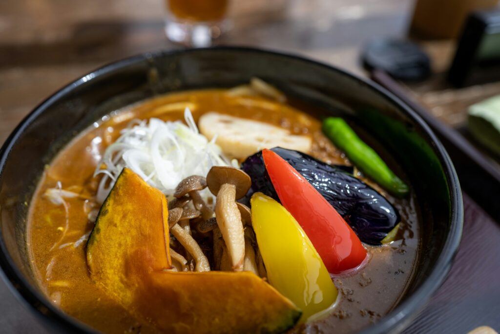 This image is a close-up of a bowl filled with a hearty, orange-colored stew or curry, featuring large chunks of potato, leafy green vegetables, and chickpeas, garnished with fresh cilantro and sesame seeds.