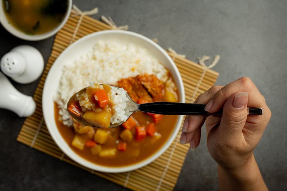 A spoon full of Japanese Soup Curry above its plate that's laid on a bamboo mat with miso soup on the side.