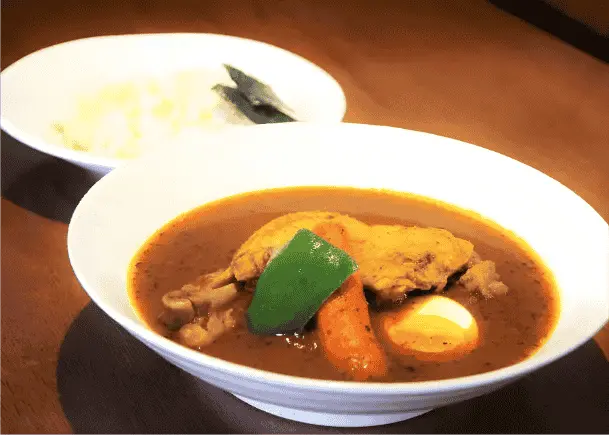 A bowl of Soup Curry sitting on top of a glossy brown table as the light shines, showcasing the delicacy that’s beautifully prepared.