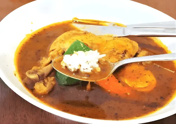 A close up photo of a Japanese Soup Curry bowl with a spoon full of the delicacy as it rests inside the bowl.