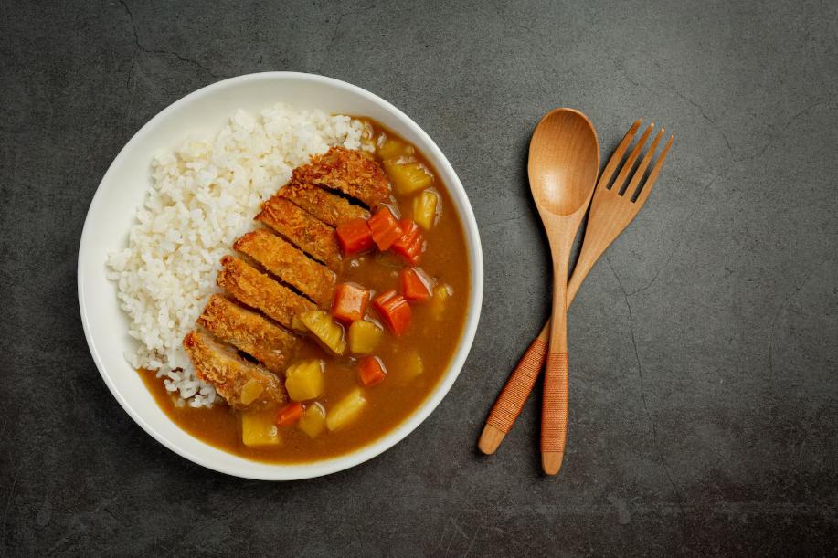 A Japanese Soup Curry beautifully presented on an ash table accompanied by wooden utensils.