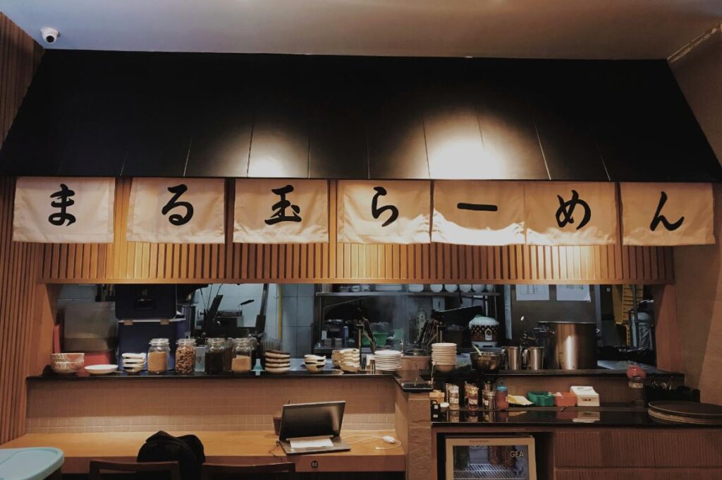 A nighttime view of an izakaya style Japanese restaurant as the light illuminates the writing on top of the countertop.