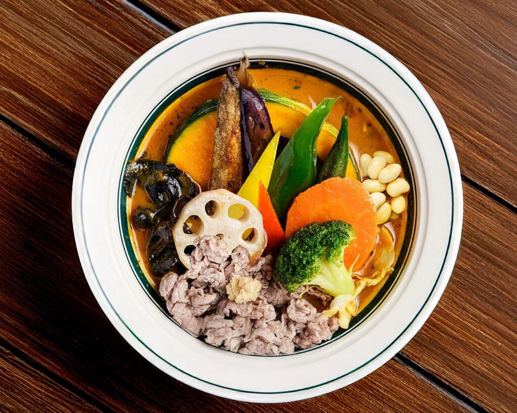 Hokkaido-style soup curry topped with generously sized vegetables, including carrots, potatoes, and leafy greens, immersed in a rich, aromatic broth that highlights the dish’s bold flavours and rustic charm.