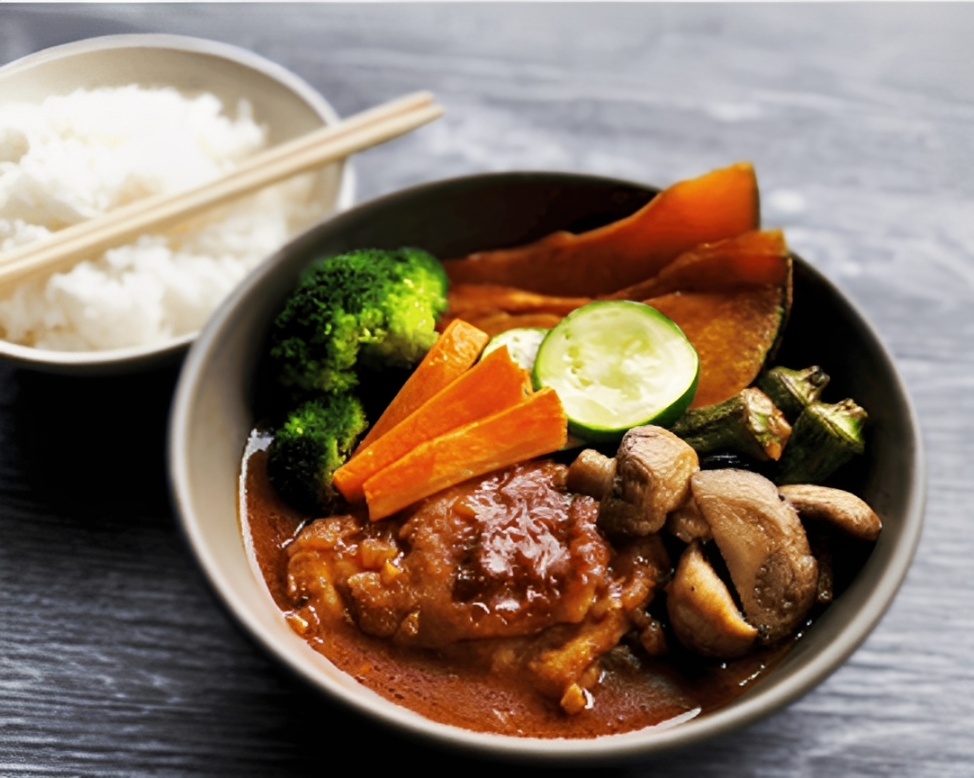 A steaming bowl of Hokkaido soup curry, rich in spices and fresh ingredients, served with rice, offering a hearty and comforting Japanese dish