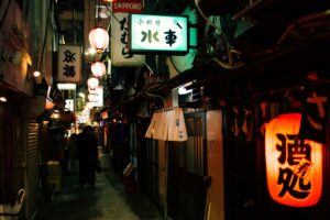 A glowing red paper lantern hanging outside a traditional izakaya restaurant, softly lighting the entrance and creating a warm, inviting street atmosphere at night.
