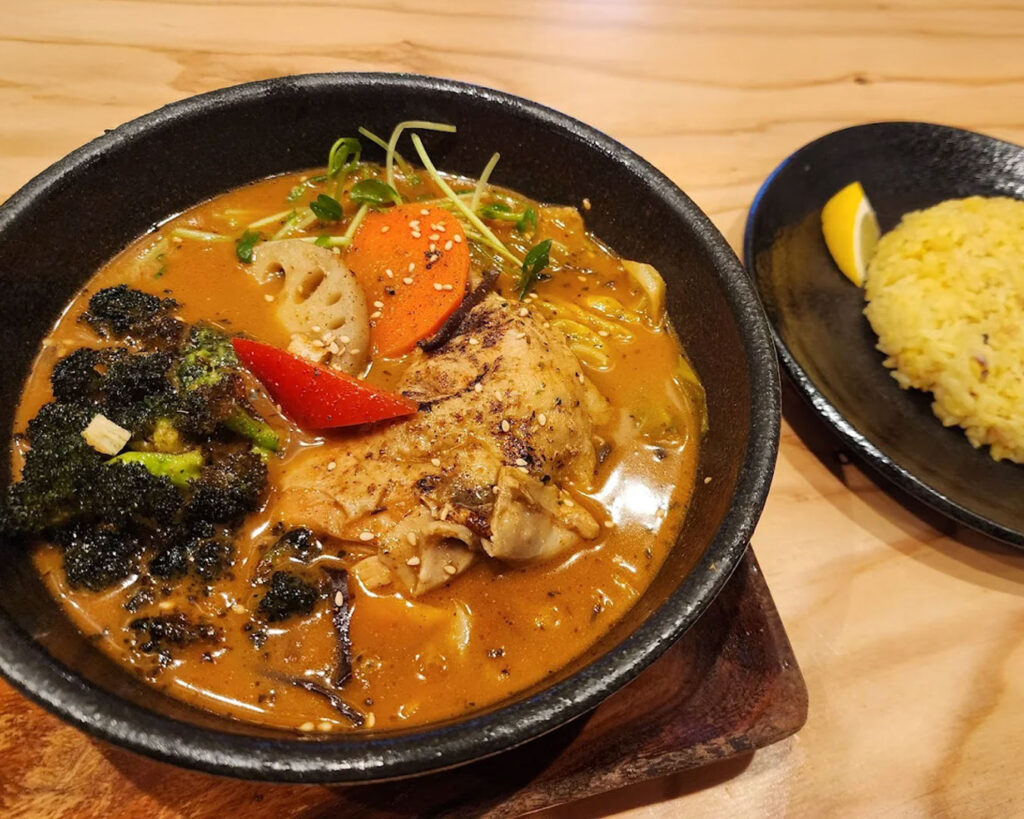 A bowl of Japanese soup curry served alongside steamed rice, highlighting the contrast between rich broth and fluffy grains.