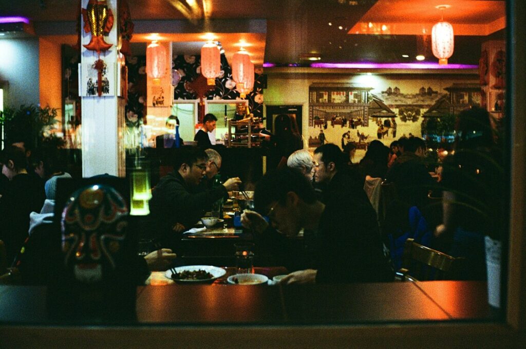A group of diners seated around a wooden table inside an izakaya, enjoying shared dishes and drinks in a lively yet cosy Japanese dining setting.