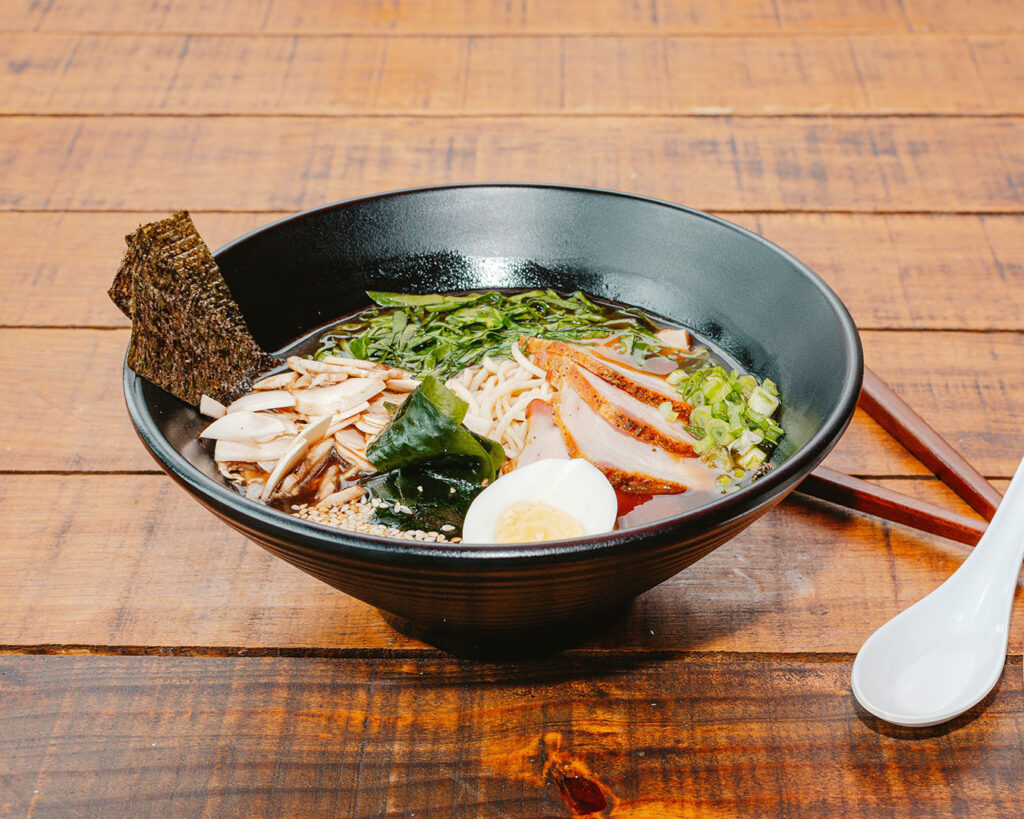 A bowl of ramen sits on the table, topped with garnishes and served hot, ready to be enjoyed in a relaxed izakaya-style atmosphere.
