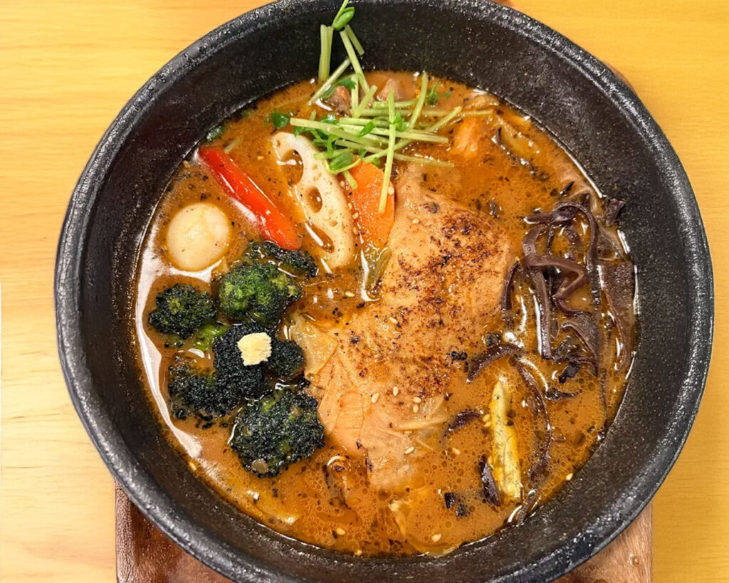 Traditional Hokkaido-style soup curry with tender vegetables and meat, presented in a deep bowl with vibrant, spiced broth.