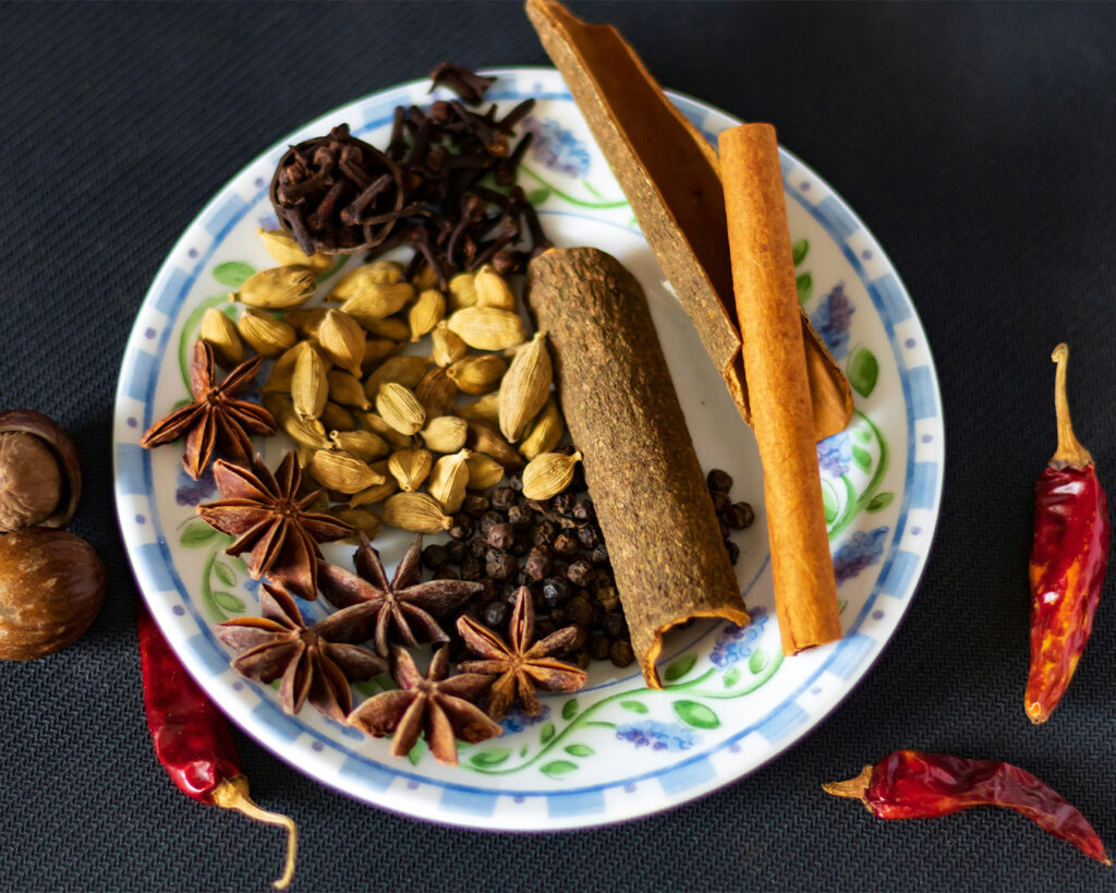 Assorted whole spices including cumin seeds, coriander seeds, cloves, cinnamon sticks, and green cardamom arranged neatly.
