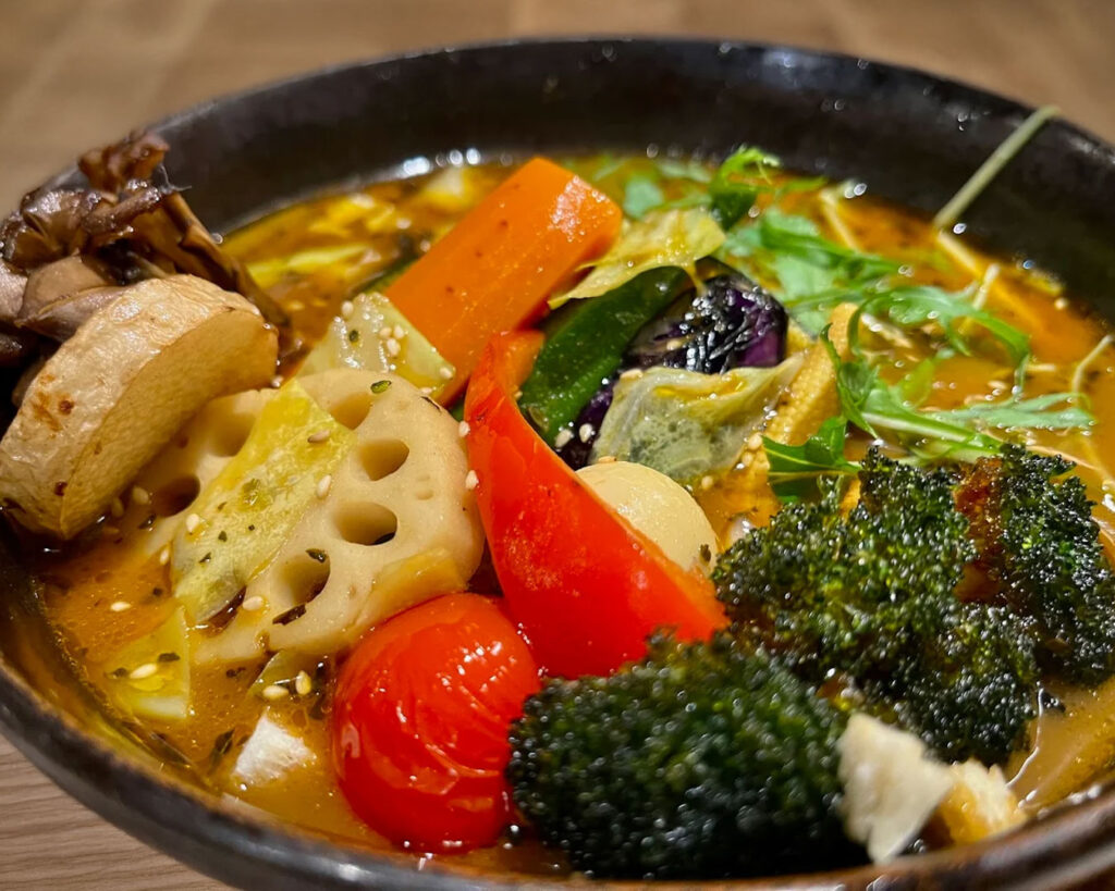 lose-up view of Hokkaido soup curry showcasing rich colour, floating herbs, and tender vegetables in spiced soup.