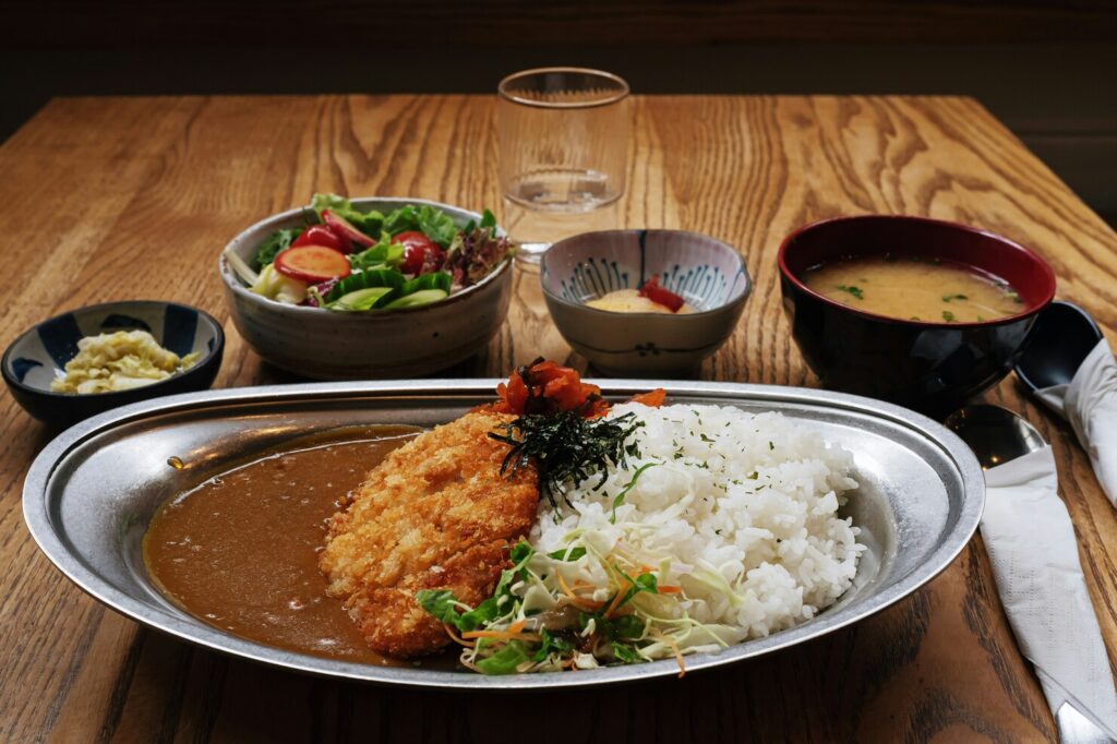 Japanese curry rice plated neatly with fluffy white rice, accompanied by a carefully prepared side dish that adds balance and contrast to the deep, savoury curry.