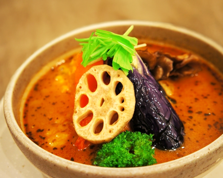 A close-up view of a single bowl of Hokkaido soup curry, featuring a clear yet flavourful broth, tender proteins, and fresh vegetables arranged with care.