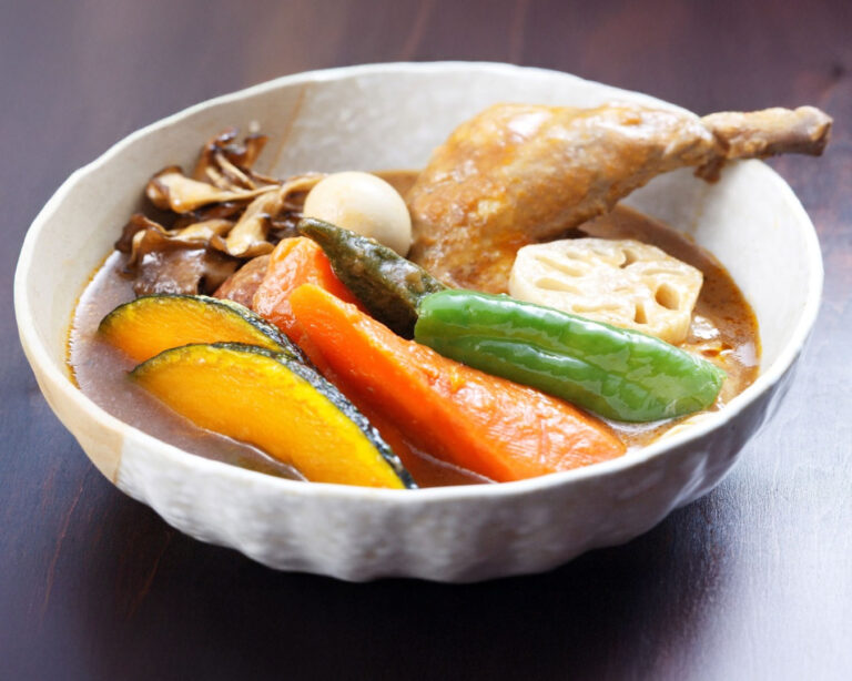 A bowl of Hokkaido soup curry with a braised chicken leg, quail egg, maitake mushrooms, lotus root, and thick-cut roasted pumpkin and carrots.