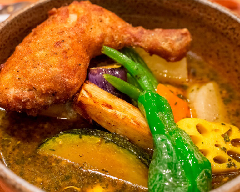 Crispy fried chicken leg with roasted pumpkin, lotus root, and green beans in a rich Japanese soup curry broth.