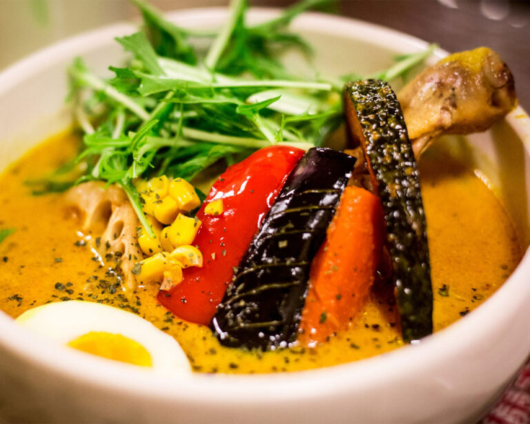 Close-up of a creamy yellow coconut curry with chicken, sliced lotus root, red peppers, and fresh green herbs.