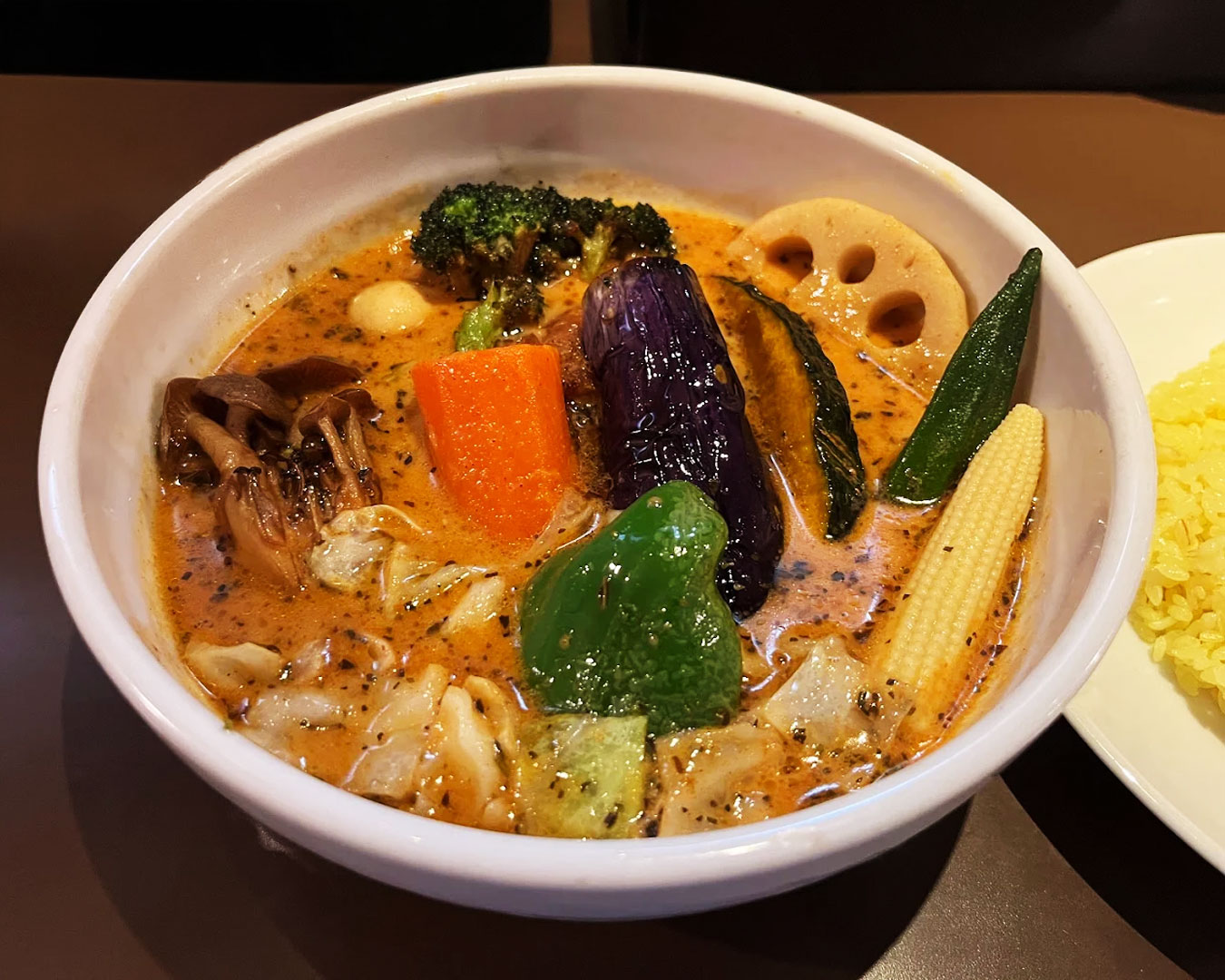 A bowl of Hokkaido-style soup curry placed on a wooden table, served with tender chicken, colourful vegetables, and aromatic broth, creating a warm and inviting dining scene.