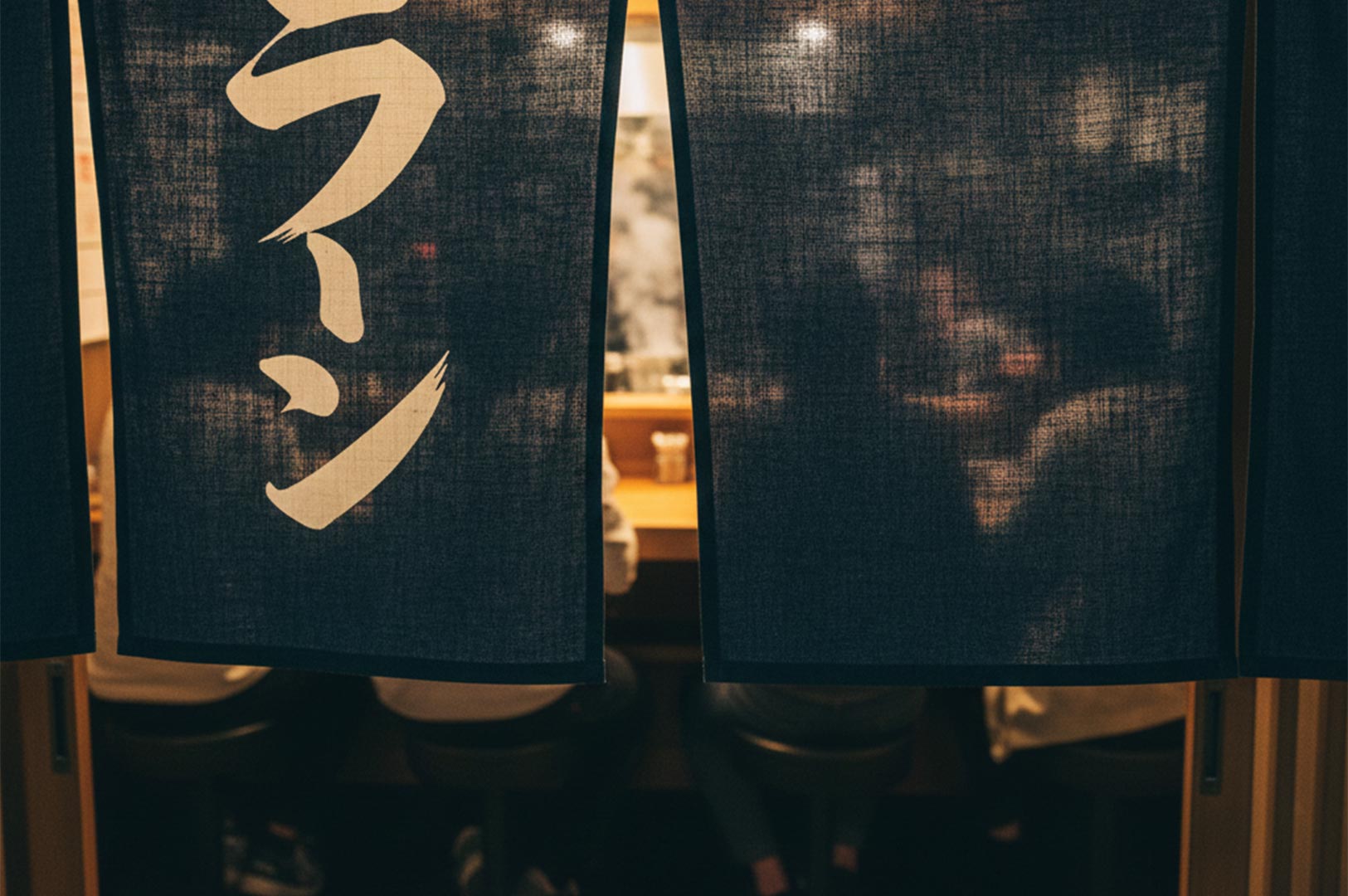 A dark blue traditional Japanese noren curtain with "Ramen" written in white calligraphy hanging at the entrance of a restaurant.