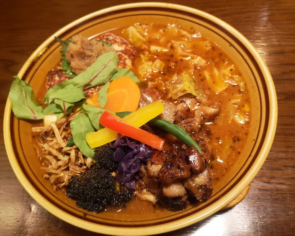 A full bowl of soup curry presented on the table, inviting and warm with visible herbs and spices.