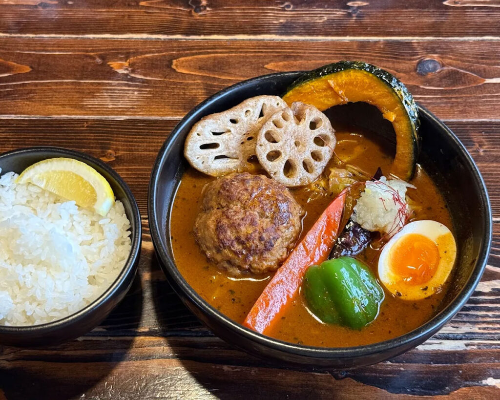 A vibrant bowl of Hokkaido soup curry with tender chicken, potatoes, carrots, and boiled egg in a spiced, clear curry broth, presented in a rustic ceramic bowl.