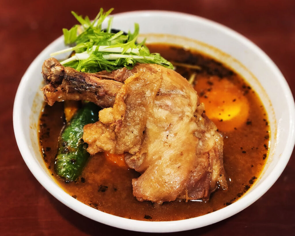 A bowl of Hokkaido soup curry with rich, spiced broth, served with rice and a variety of vegetables, showcasing the dish’s vibrant colours and comforting presentation.