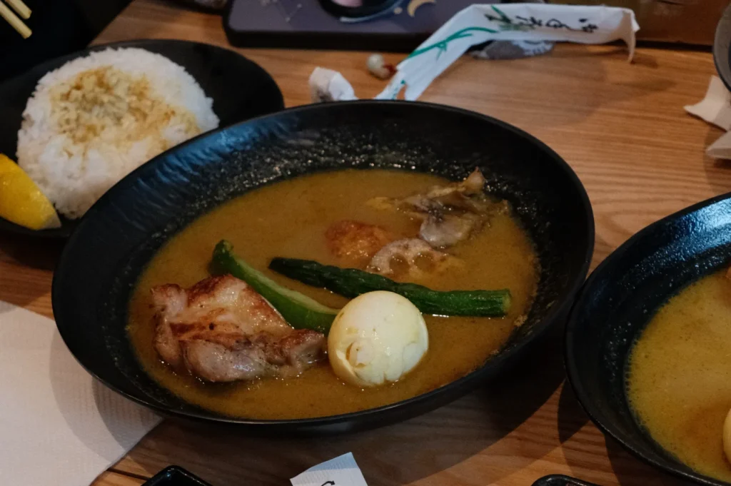 A bowl of ramen soup with sliced meat, green onions, and a soft-boiled egg, alongside a serving of rice.