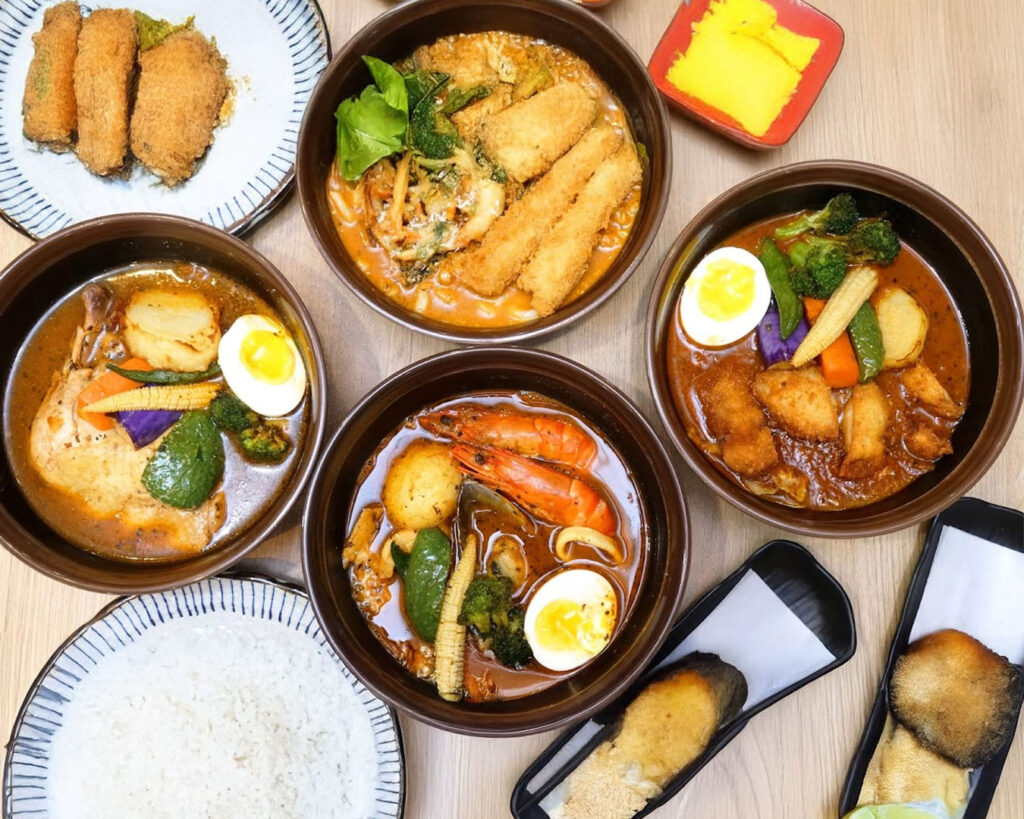 Several bowls of soup curry displayed together, each with different toppings such as chicken, seafood, and seasonal vegetables.