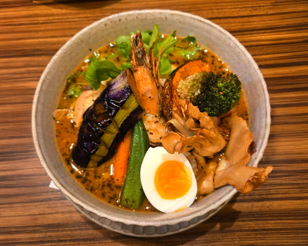 A close-up of soup curry in a ceramic bowl on the dining table, highlighting the clear broth and layered ingredients.