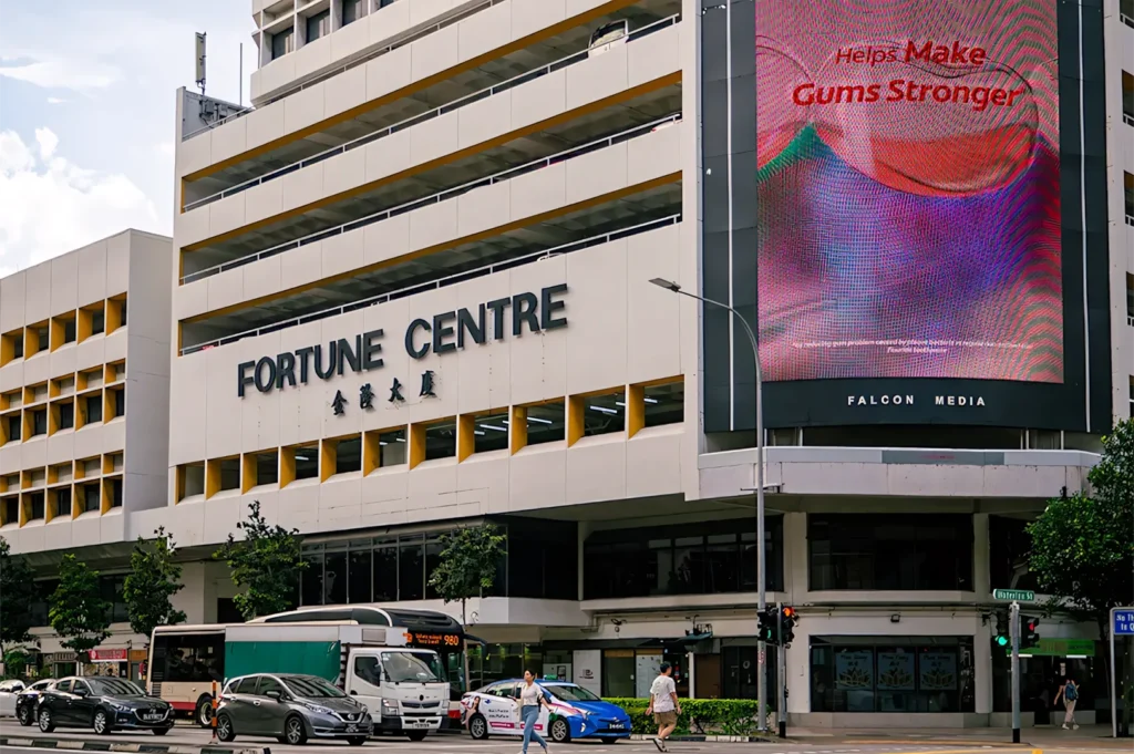 Exterior view of Fortune Centre in Singapore, showing the building facade, street-level traffic, and a large digital advertisement screen.