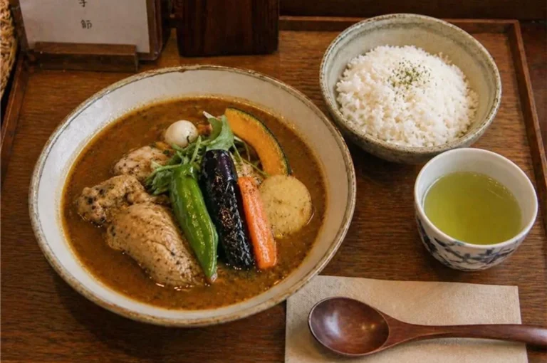 A complete Sapporo soup curry meal set with steamed rice and green tea on a wooden table.