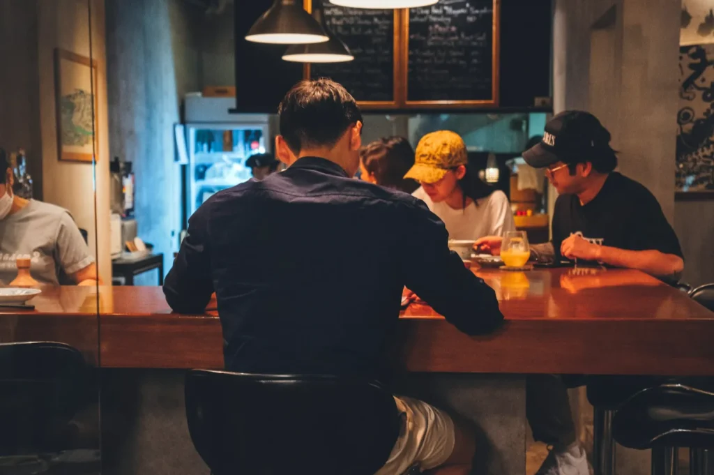 Four people sit around a cozy wooden bar in a dimly lit cafe. Warm, ambient lighting creates an intimate atmosphere as they engage in conversation.