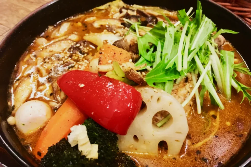 A bowl of savory vegetable soup featuring red bell pepper, carrots, lotus root, mushrooms, and fresh greens, creating a vibrant and hearty dish.