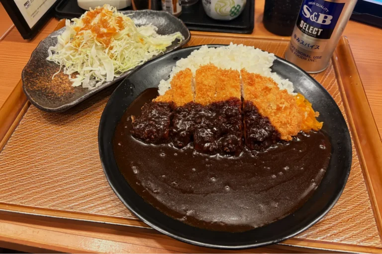 A mouth-watering plate of Japanese curry with crispy katsu, rich brown sauce, and rice. Side salad with shredded cabbage. Comforting, savory meal.