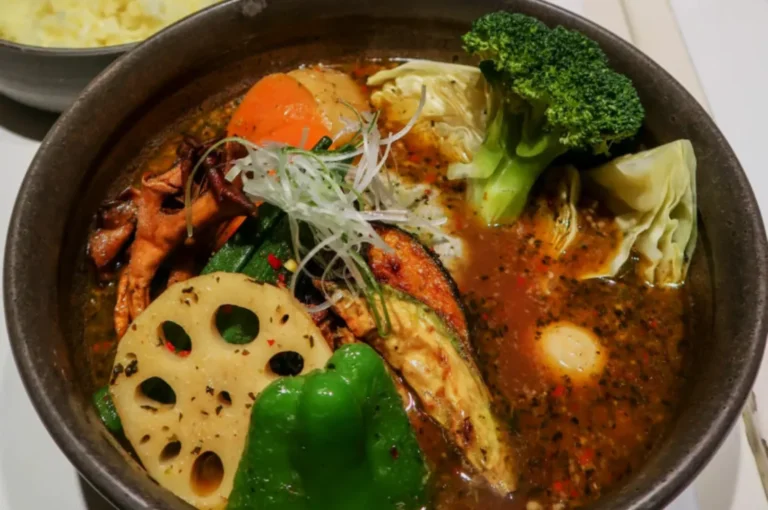 A vibrant bowl of vegetable soup curry with broccoli, lotus root, carrot, bell pepper, mushrooms, and microgreens in rich broth, exuding warmth.