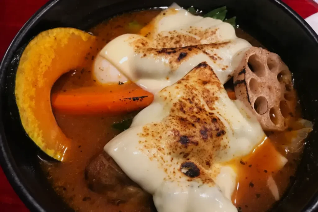 A steaming bowl of soup with melted cheese, featuring vibrant pumpkin, carrot, and lotus root slices, creates a warm and savory vibe.