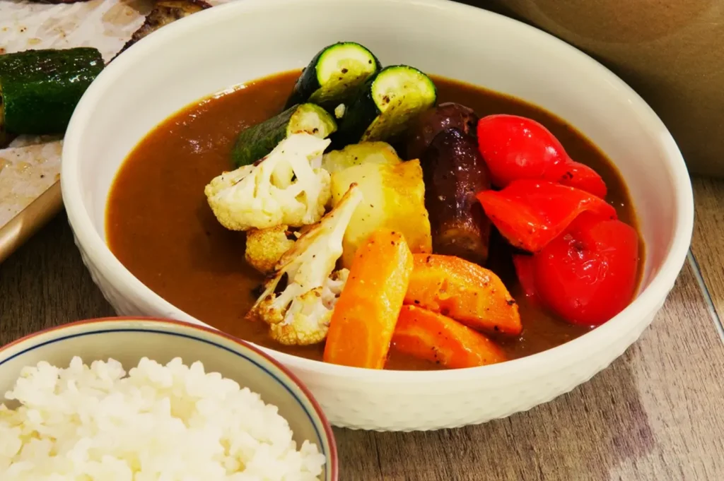Bowl of Japanese curry with colorful vegetables including zucchini, cauliflower, carrots, and red peppers. Served with white rice. Cozy and appetizing.
