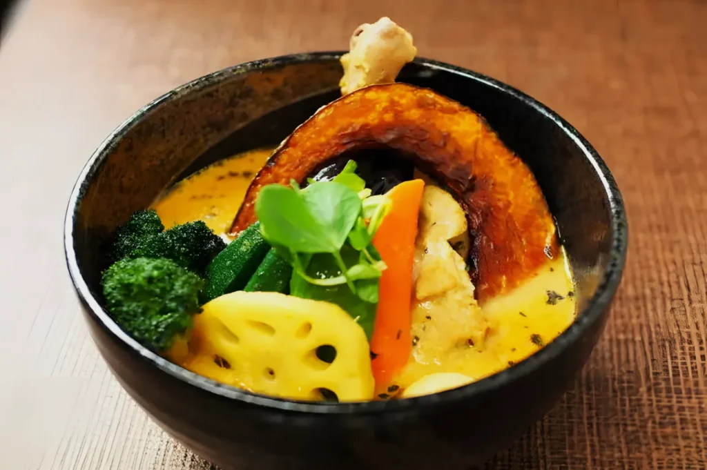 A vibrant bowl of Japanese vegetable curry featuring broccoli, lotus root, carrot, and pumpkin slice in creamy yellow sauce. Fresh, inviting, and colorful.