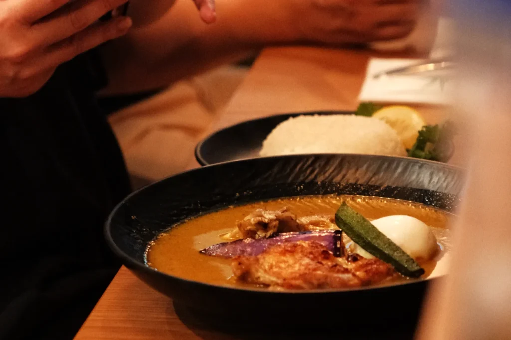 A bowl of curry with rice, garnished with sliced vegetables and a soft-boiled egg, served on a wooden table.