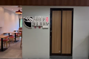 A restaurant entrance with a sign that says "SOUP CURRY," featuring an illustration related to soup curry dishes.