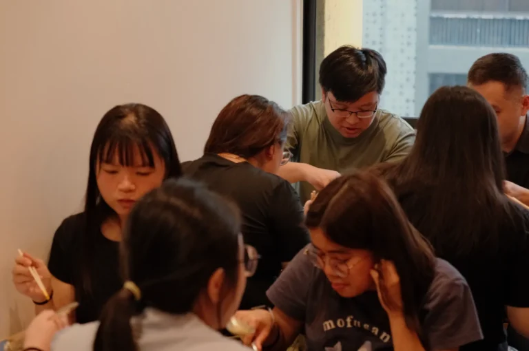 A group of people dining together at a table, some using chopsticks and others engaged in conversation.