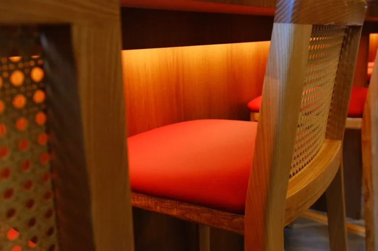 A close-up of a wooden chair with a red cushion at a table, featuring warm, ambient lighting underneath the surface.