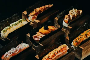 A variety of sushi and nigiri pieces artfully presented on wooden blocks. Each piece features unique toppings, such as roe, onion, and chives.