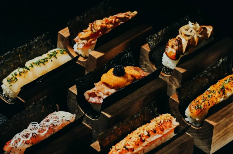 A variety of sushi and nigiri pieces artfully presented on wooden blocks. Each piece features unique toppings, such as roe, onion, and chives.