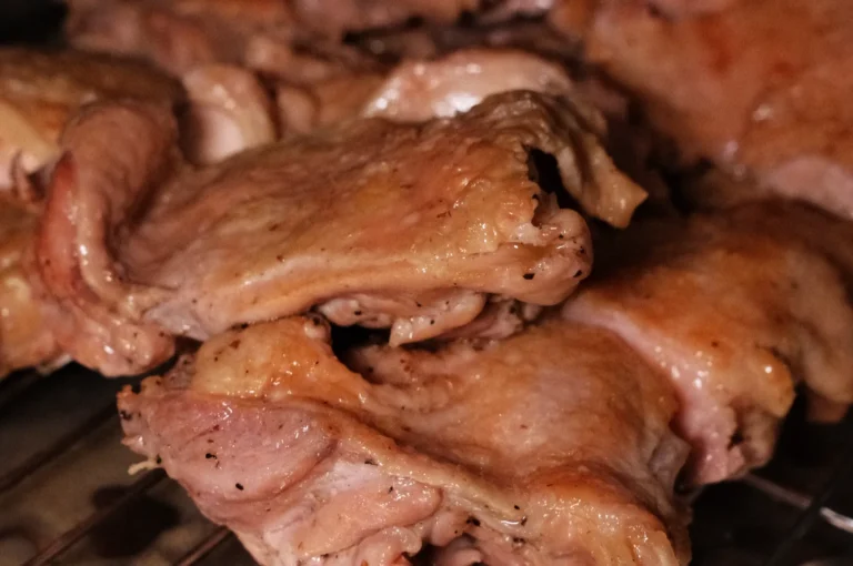 Close-up of cooked chicken thighs, golden brown and juicy, resting on a grill.