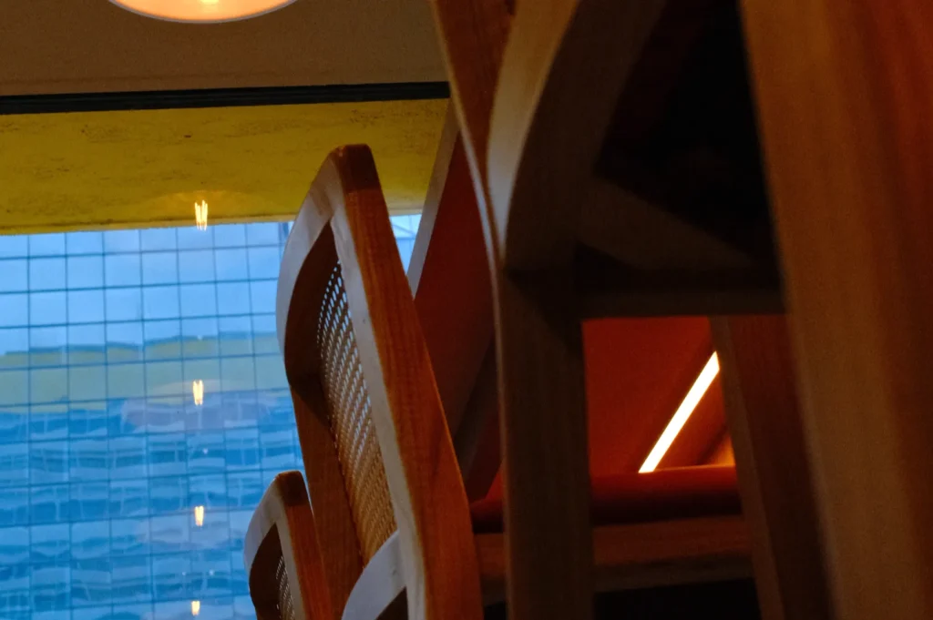 A low-angle view of wooden chairs with a blurred background of a glass building and soft lighting.