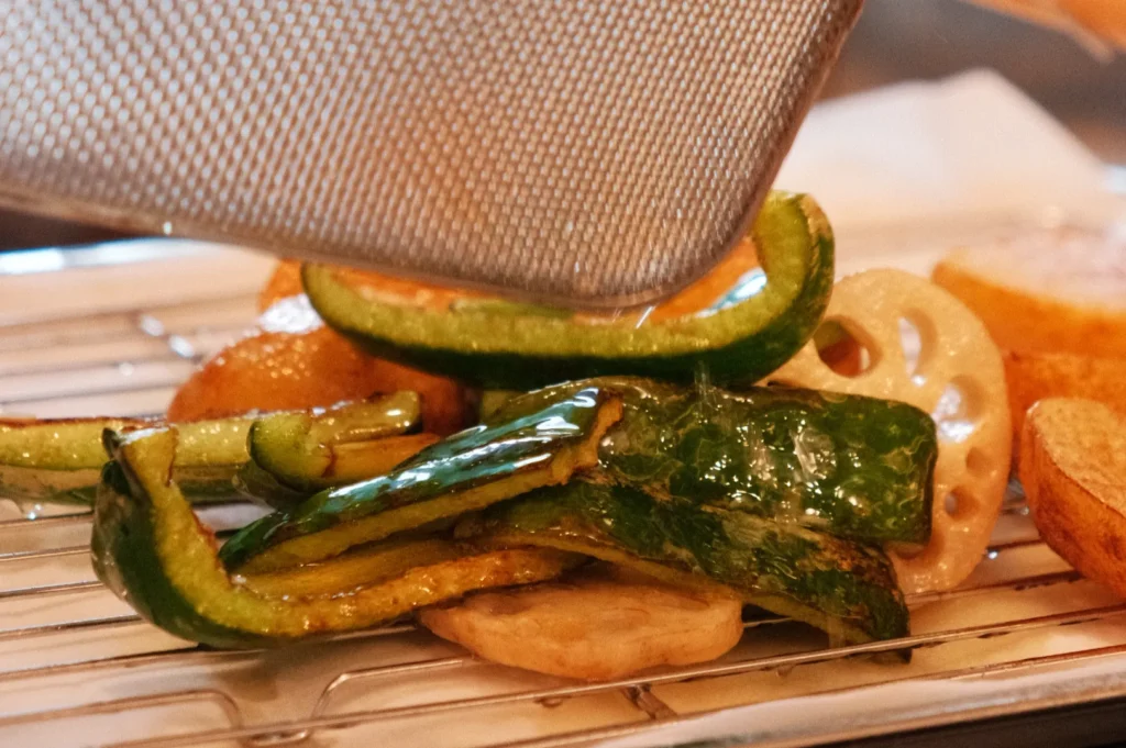 A close-up of grilled vegetables including zucchini and lotus root being served on a tray.