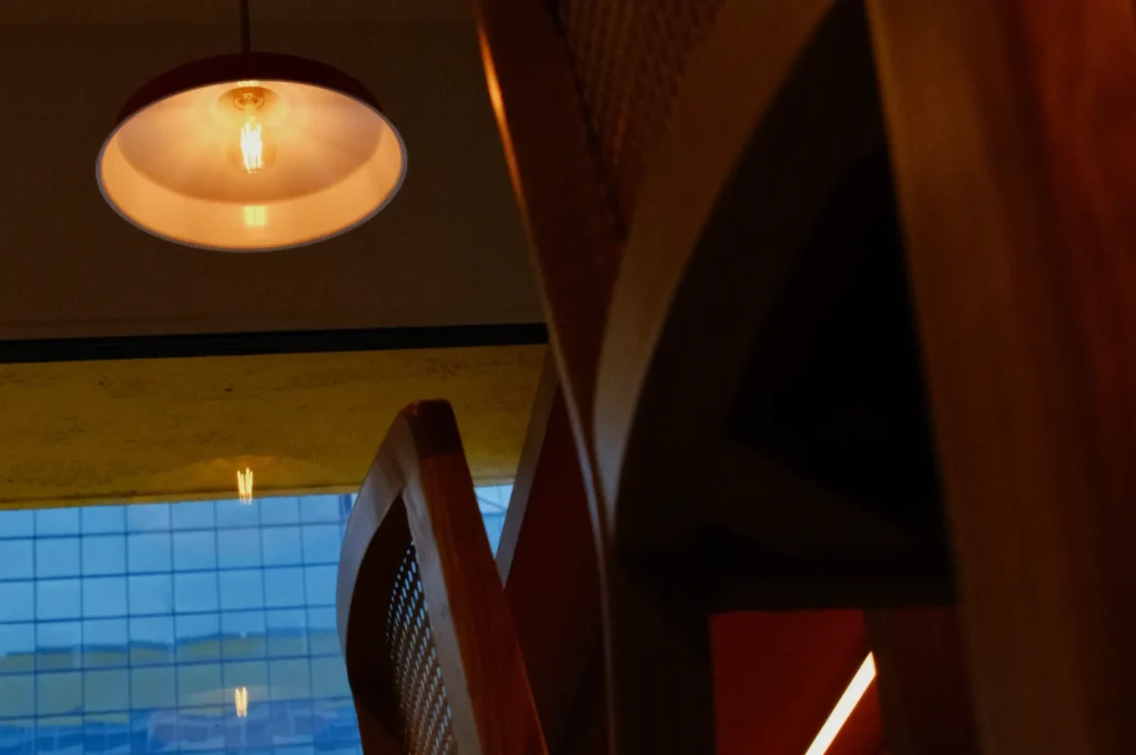 A close-up view of a wooden chair and a ceiling light fixture, with a large window in the background showing a glimpse of the outside.