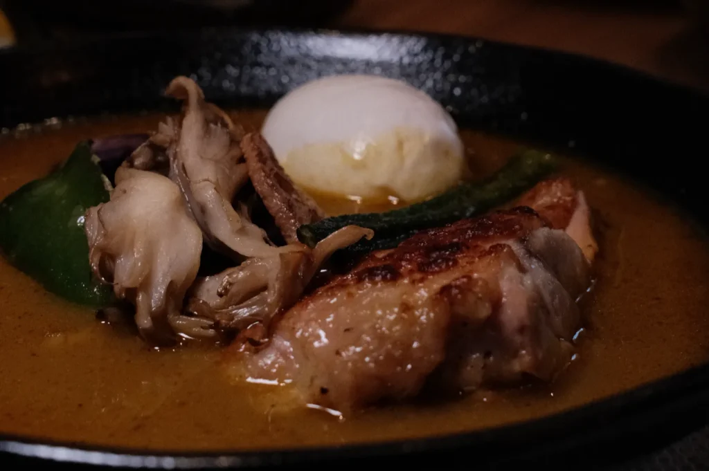 A close-up of a savory dish featuring chicken, mushrooms, and a poached egg in a rich sauce, served in a cast iron skillet with green peppers.