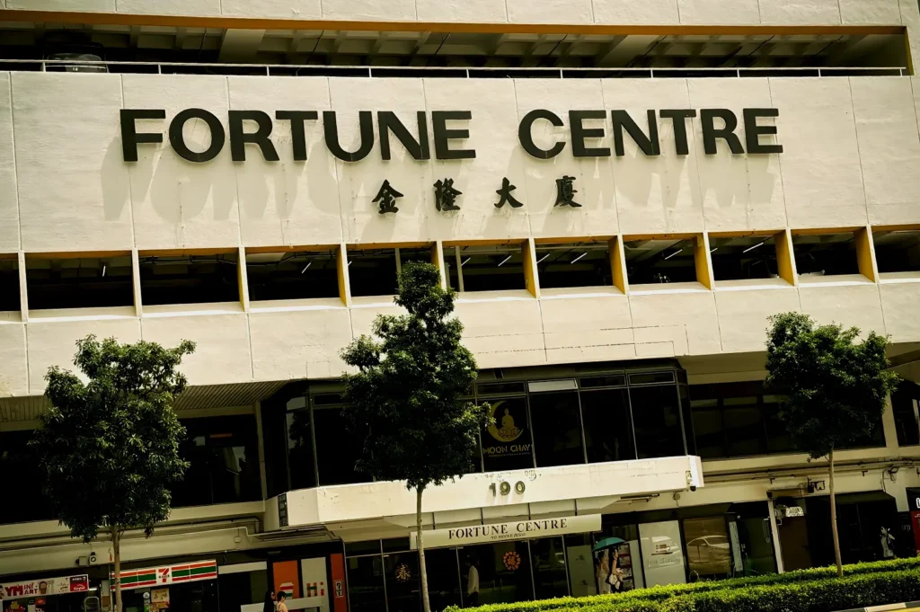 Street view of Fortune Centre, a white multi-story building with large signage. Trees line the front, and sunlight casts soft shadows, creating a calm atmosphere.